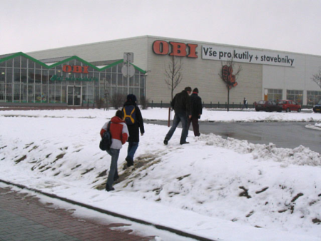 Lidé mířící do nákupního centra z nevhodně umístěné zastávky